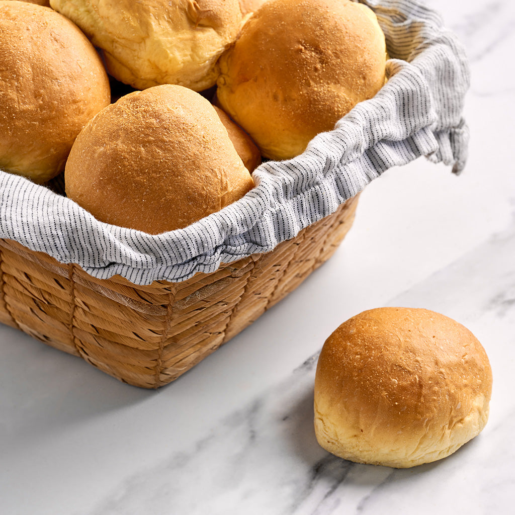 A basket filled with golden-brown baked bread rolls, with a striped cloth lining, placed on a marble surface.