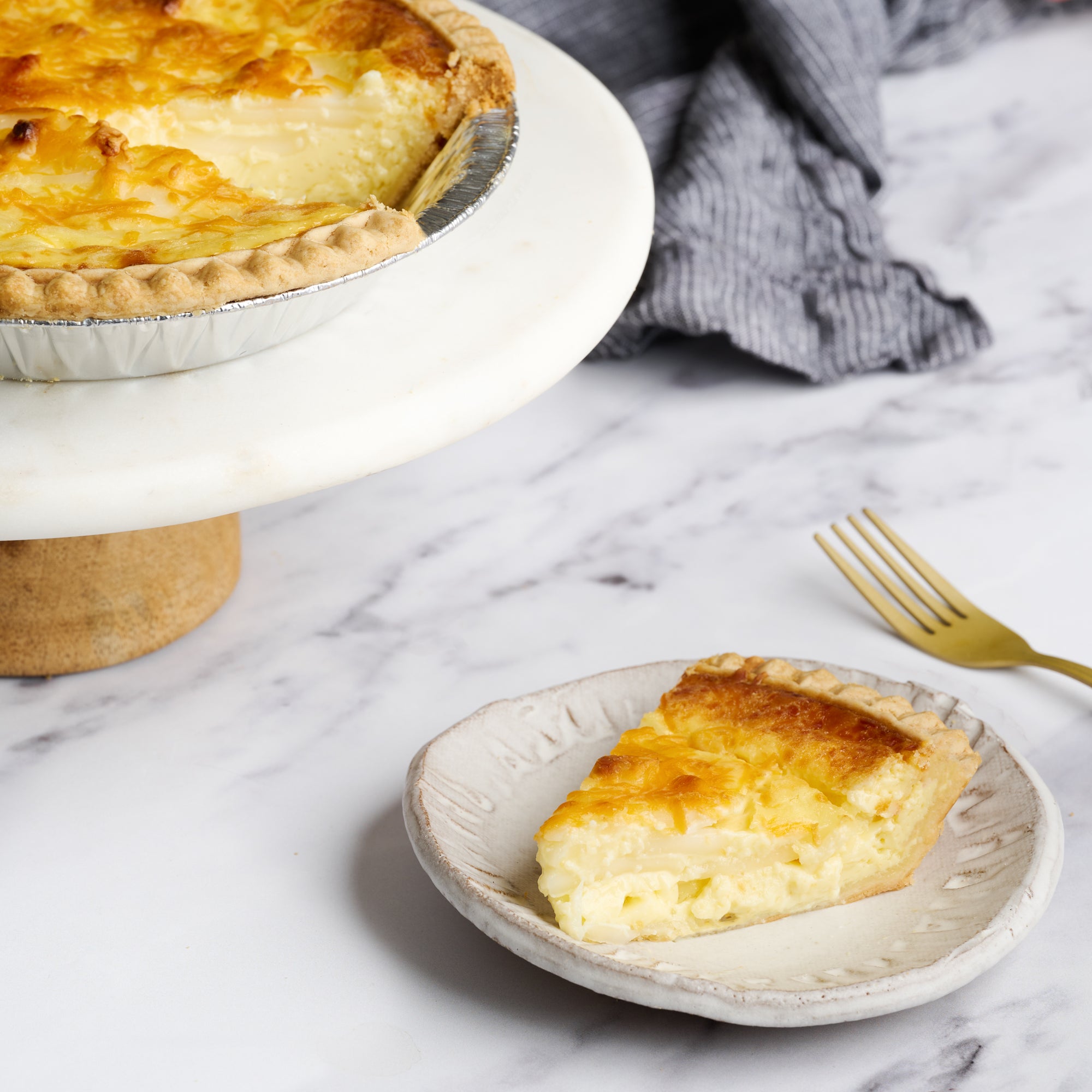 A slice of Buko Pie on a white plate with the rest of the pie in the background, displayed on a marble surface with a cloth and fork beside it.